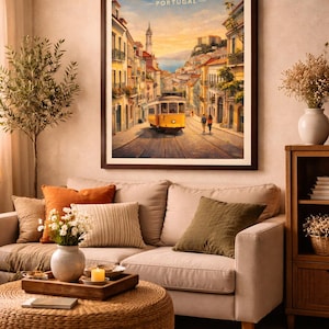 May include: A framed print of Lisbon, Portugal, hangs above a beige sofa with decorative pillows. The artwork depicts a yellow tram on a cobblestone street, with buildings lining the sides. The word "LISBON" is at the top of the print.