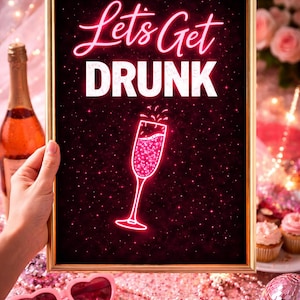 May include: A framed print with the words "Let's Get DRUNK" in pink neon lettering, with a champagne glass illustration. The background is a dark pink with sparkling stars. A bottle of champagne and pink heart-shaped sunglasses are also visible.