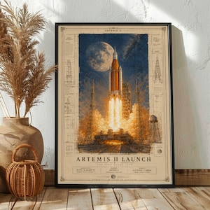 May include: A framed print depicting the Artemis II launch. The artwork features a rocket launching into space against a backdrop of a full moon and a blue sky. The print includes technical diagrams and the text "Artemis II Launch".