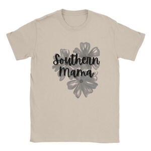 May include: A beige t-shirt featuring the text "Southern Mama" in a black script font, accompanied by a cluster of gray floral illustrations. The shirt has a crew neck and short sleeves.
