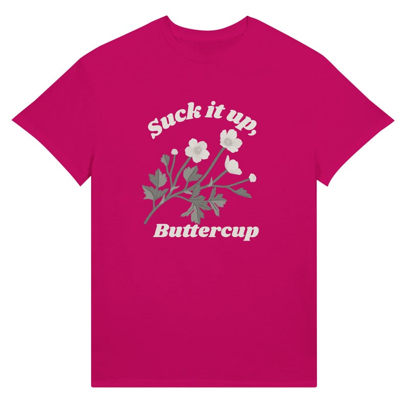May include: A magenta t-shirt featuring the text "Suck it up, Buttercup" in white script above a floral illustration. The design includes white flowers and green leaves.