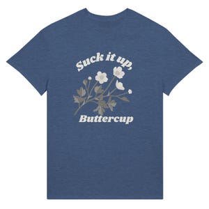 May include: Blue t-shirt with the text "Suck it up, Buttercup" in a white, vintage-style font. The shirt features a floral design with white flowers and gray leaves. The tee is a casual wear item.