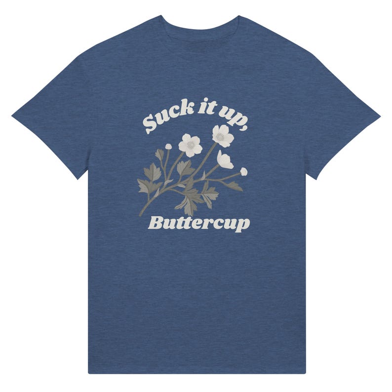 May include: Blue t-shirt with the text "Suck it up, Buttercup" in a white, vintage-style font. The shirt features a floral design with white flowers and gray leaves. The tee is a casual wear item.
