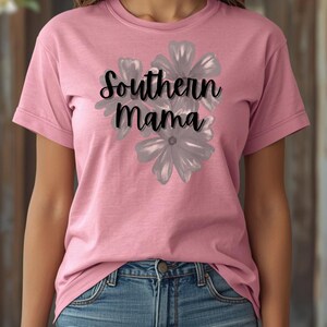 May include: A pink t-shirt with the text "Southern Mama" in black script, overlaid on a gray floral design. The shirt is short-sleeved and worn with blue jeans.