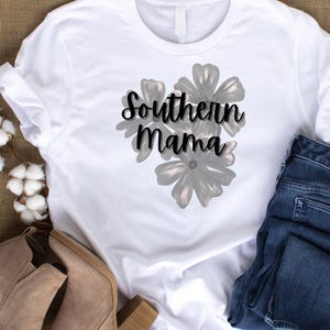 May include: White t-shirt with the text "Southern Mama" in a script font, overlaying a floral design. The shirt is paired with blue jeans and tan ankle boots, suggesting a casual, everyday style.