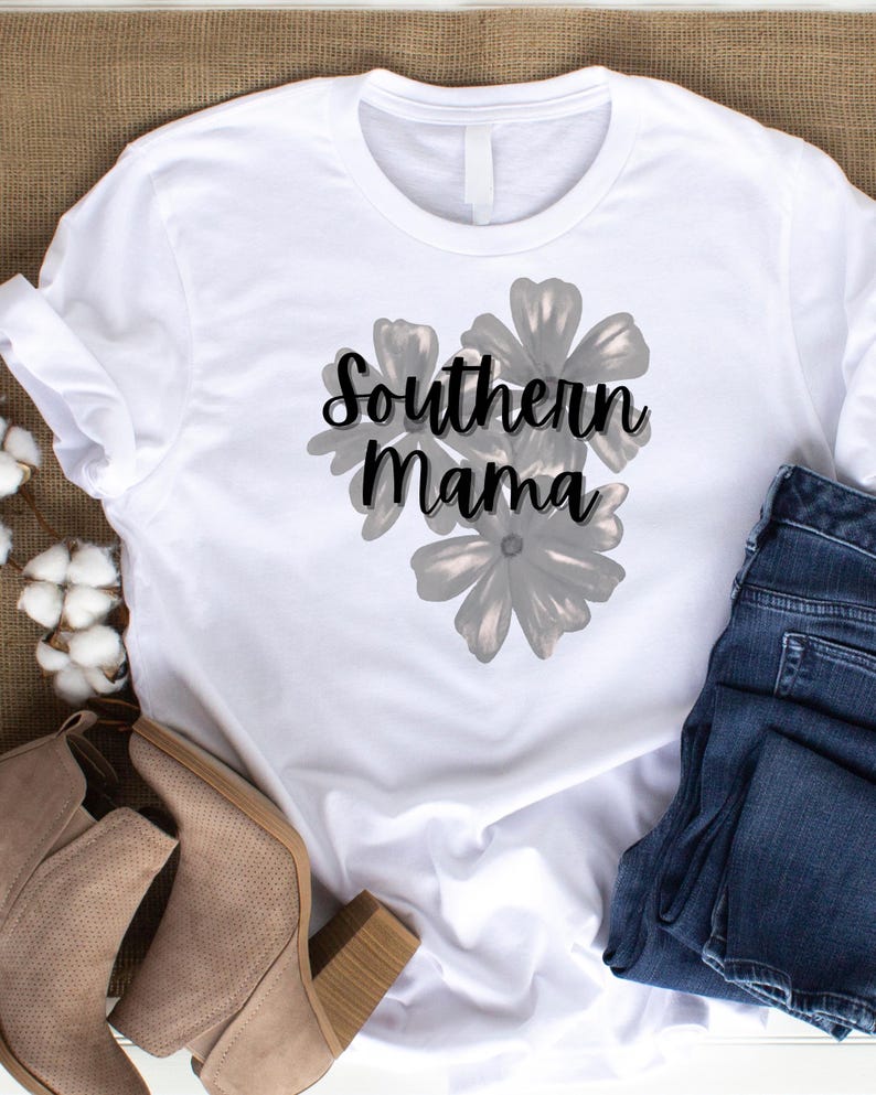 May include: White t-shirt with the text "Southern Mama" in a script font, overlaying a floral design. The shirt is paired with blue jeans and tan ankle boots, suggesting a casual, everyday style.
