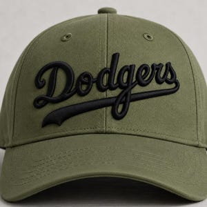 May include: An olive green baseball cap featuring the word Dodgers embroidered in black script across the front. The cap has a structured crown, a curved brim, and stitched eyelets on the top panels for ventilation and a classic athletic look.