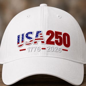 Op de afbeelding: Een witte baseballpet met geborduurde tekst op de voorzijde. De letters USA zijn gevuld met een rood, wit en blauw Amerikaans vlagpatroon, gevolgd door het rode getal 250. Daaronder zijn de jaartallen 1776-2026 in witte draad geborduurd.