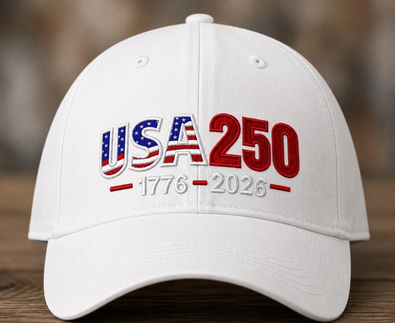 Op de afbeelding: Een witte baseballpet met geborduurde tekst op de voorzijde. De letters USA zijn gevuld met een rood, wit en blauw Amerikaans vlagpatroon, gevolgd door het rode getal 250. Daaronder zijn de jaartallen 1776-2026 in witte draad geborduurd.
