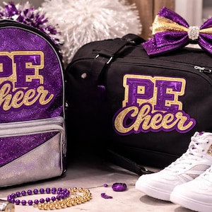 May include: A purple glitter backpack and black duffel bag with "PE Cheer" lettering in gold and purple. White high-top sneakers with gold glitter accents are next to the bags. A purple and gold bow and jewelry complete the cheerleading theme.