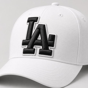 May include: White baseball cap with a curved brim. The cap features a black and white embroidered "LA" logo on the front. The hat has a structured crown and a button on top. The design is simple and classic.