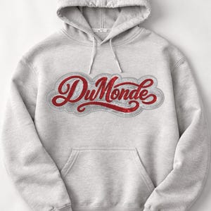 May include: A light gray hooded sweatshirt with a front pocket and a drawstring hood. The sweatshirt features the red text "Du Monde" in a decorative font, outlined with silver stitching.