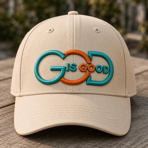 Op de afbeelding: Beige baseballpet met de geborduurde tekst "GOD IS GOOD" in teal en oranje. De pet heeft een gebogen klep en een knoop aan de bovenkant. De hoed is gemaakt van een zachte stof en is geschikt voor vrijetijdskleding.