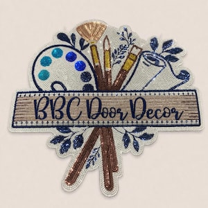 May include: Embroidered door decor featuring art supplies. The design includes a paint palette, paintbrushes, and a roll of paper, all embellished with beads. The text "BBC Door Decor" is displayed on a wooden-style banner.