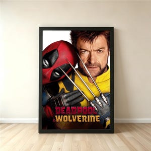 May include: Framed poster featuring Deadpool in a red mask and Wolverine with metal claws. The poster has the words "Deadpool & Wolverine" in red and white text. The characters are set against a yellow and black background.
