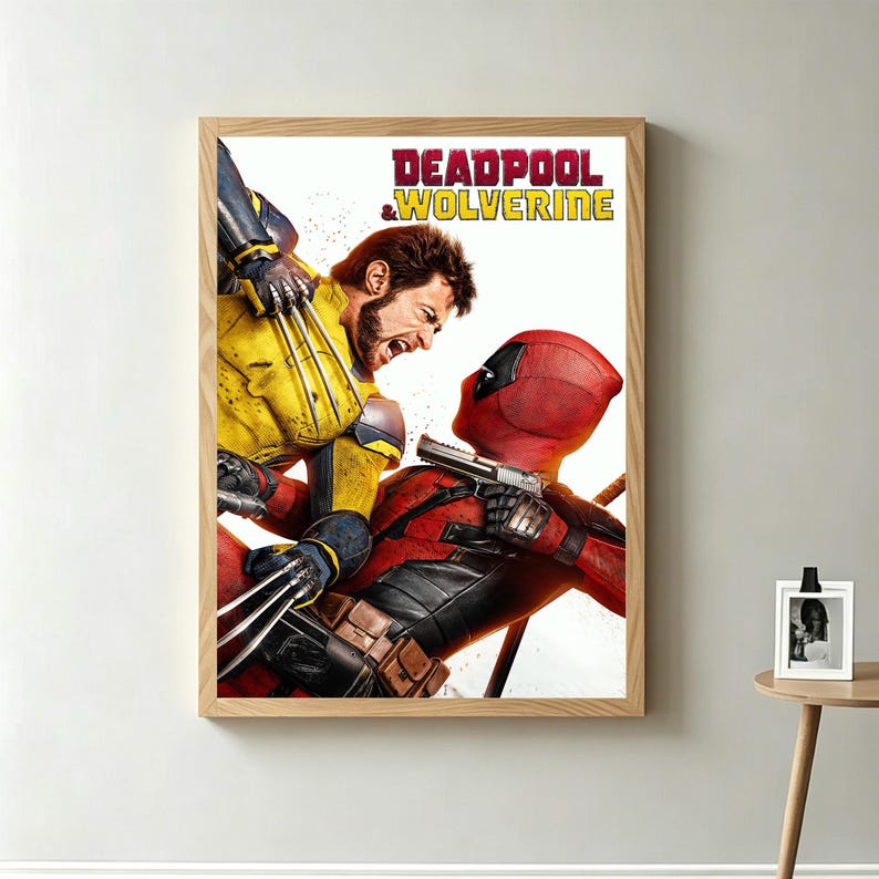 May include: A framed poster featuring a dynamic action scene from the movie "Deadpool & Wolverine." The artwork depicts Wolverine in a yellow and blue suit clashing with Deadpool in a red suit. The title text is in red and yellow.