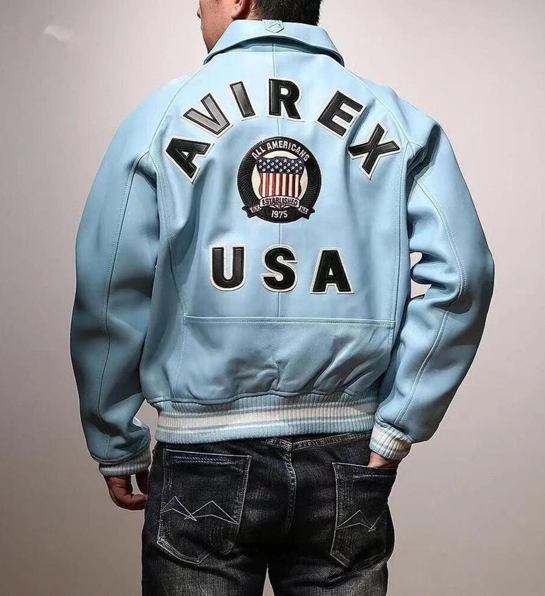 May include: Light blue leather jacket with the word "AVIREX" across the shoulders and "USA" on the lower back. A circular patch with the American flag and the words "ALL AMERICANS ESTABLISHED 1975" is centered on the back.