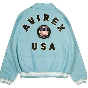May include: Light blue jacket with the text "AVIREX" and "USA" on the back. The jacket features a patch with the words "All Americans" and a design of the American flag. The jacket has white and light blue striped cuffs and hem.