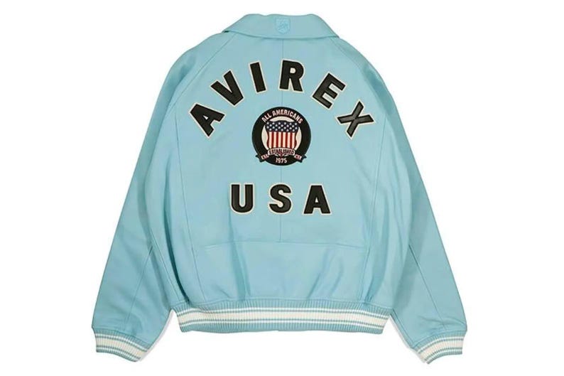 May include: Light blue jacket with the text "AVIREX" and "USA" on the back. The jacket features a patch with the words "All Americans" and a design of the American flag. The jacket has white and light blue striped cuffs and hem.