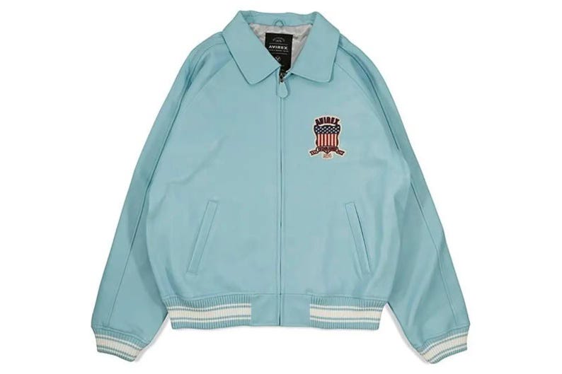 May include: A light blue jacket with a collared neckline and a zipper closure. The jacket features a patch with an American flag design and the brand name. The cuffs and hem have white and light blue striped detailing.