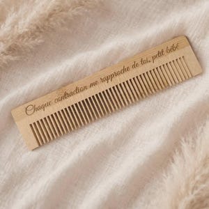 Peut inclure: Un peigne en bois de couleur claire doté d'une série de dents fines sur un côté. La surface du peigne est gravée avec le texte "Chaque contraction me rapproche de toi, petit bébé," écrit dans une police d'écriture cursive et élégante.