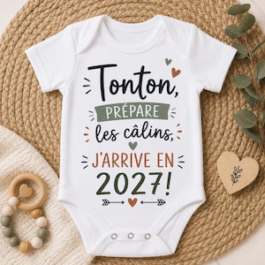 Peut inclure: Un body pour bébé blanc à manches courtes avec le texte noir, vert et orange "Tonton, PRÉPARE les câlins, J'ARRIVE EN 2027!" agrémenté de petits cœurs et de flèches. Le vêtement possède une encolure ronde et trois boutons-pression en métal.