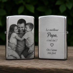 Peut inclure: Un briquet argenté avec une photo en noir et blanc d'un père et de ses deux enfants. L'autre face porte l'inscription "Le meilleur Papa, c'est toi !" avec un cœur et "On t'aime très fort."