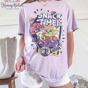 Puede incluir: Camiseta lila claro con el texto "SNACK TIME!" y un gr&aacute;fico de Grogu de The Mandalorian. El gr&aacute;fico incluye a Grogu rodeado de bayas moradas y rojas, con las palabras "Bounty Hunters".