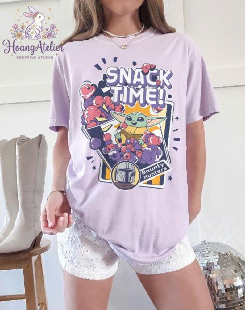Puede incluir: Camiseta lila claro con el texto "SNACK TIME!" y un gr&aacute;fico de Grogu de The Mandalorian. El gr&aacute;fico incluye a Grogu rodeado de bayas moradas y rojas, con las palabras "Bounty Hunters".