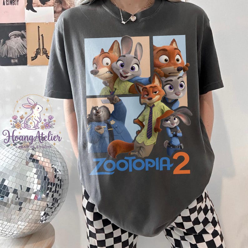 K&ouml;nnte beinhalten: Dunkelgraues T-Shirt mit einer farbenfrohen Grafik von Charakteren aus dem Animationsfilm "Zoomania". Das Design enth&auml;lt den Text "Zoomania 2" in Blau und Orange. Ein l&auml;ssiges Kleidungsst&uuml;ck.