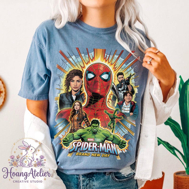 May include: Blue t-shirt featuring a graphic of Spider-Man and other Marvel characters. The design includes the text "SPIDER-MAN BRAND NEW DAY". The shirt is a light blue color.