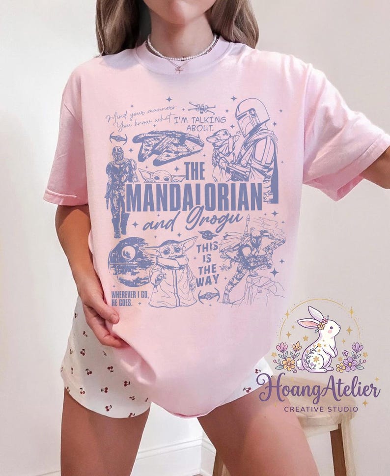 Puede incluir: Camiseta rosa claro con un dise&ntilde;o gr&aacute;fico que presenta el texto "The Mandalorian and Grogu". El dise&ntilde;o incluye ilustraciones de personajes y elementos de la serie Star Wars. La camiseta tiene mangas cortas.