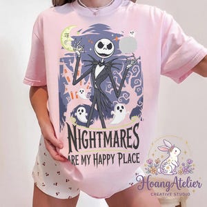 May include: Pale pink t-shirt with a graphic of Jack Skellington from The Nightmare Before Christmas. The design includes a moon, ghosts, and the text "NIGHTMARES ARE MY HAPPY PLACE."