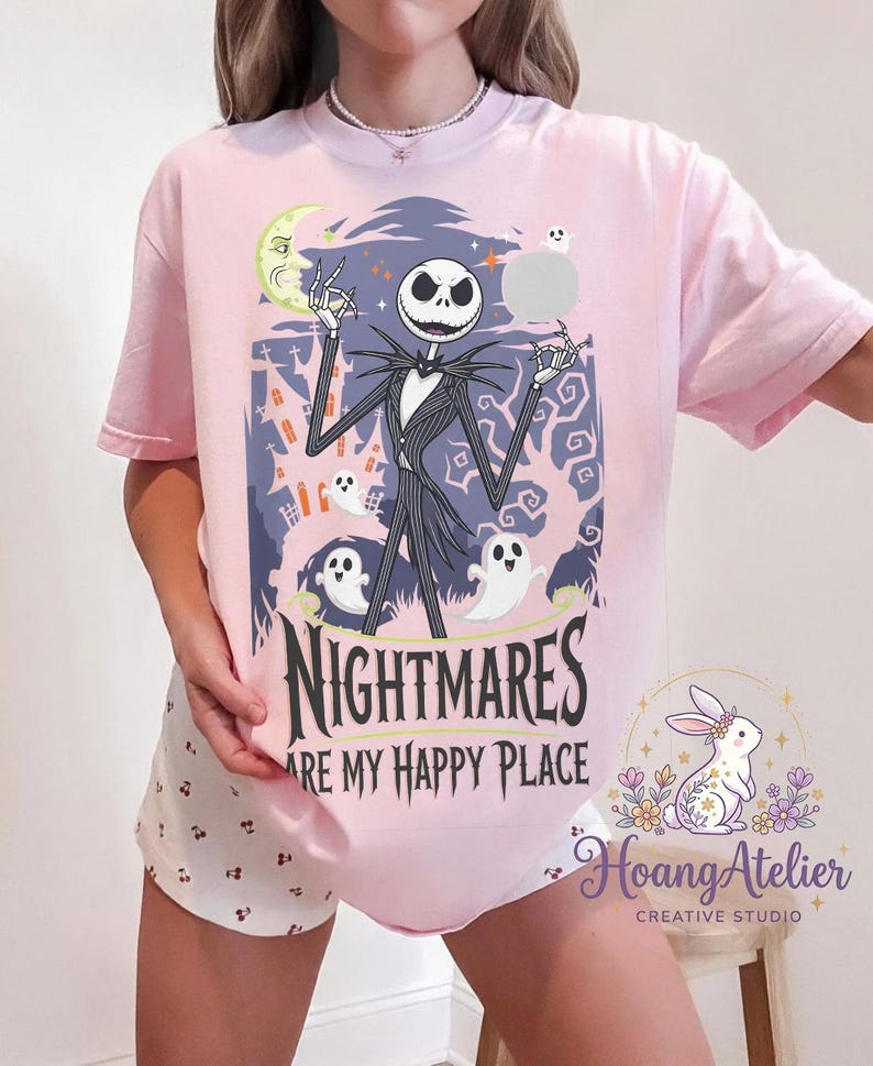 May include: Pale pink t-shirt with a graphic of Jack Skellington from The Nightmare Before Christmas. The design includes a moon, ghosts, and the text "NIGHTMARES ARE MY HAPPY PLACE."