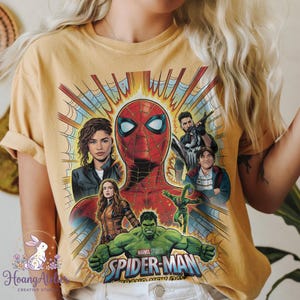 May include: Mustard yellow t-shirt featuring a graphic of Spider-Man and other Marvel characters. The design includes Spider-Man's face, Hulk, and other characters from the movie. The words "Marvel Studios Spider-Man" are also visible.