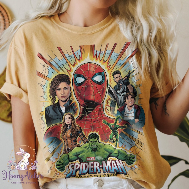 May include: Mustard yellow t-shirt featuring a graphic of Spider-Man and other Marvel characters. The design includes Spider-Man's face, Hulk, and other characters from the movie. The words "Marvel Studios Spider-Man" are also visible.