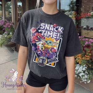 Puede incluir: Camiseta gris oscuro con la frase "SNACK TIME!" y un gr&aacute;fico de un personaje alien&iacute;gena verde rodeado de snacks morados y rojos. La camiseta tambi&eacute;n incluye las palabras "Bounty Hunters" y un dise&ntilde;o de casco.