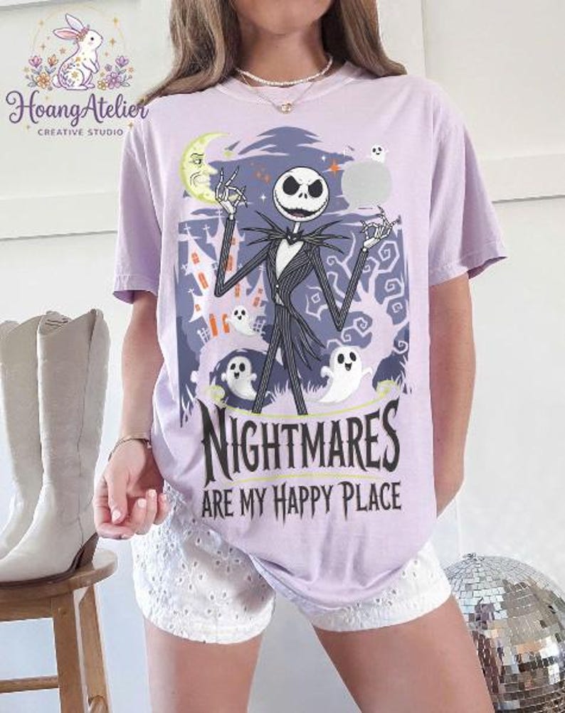 May include: A lilac t-shirt with a graphic of Jack Skellington from The Nightmare Before Christmas. The design includes ghosts, a moon, and the text "Nightmares are my happy place."