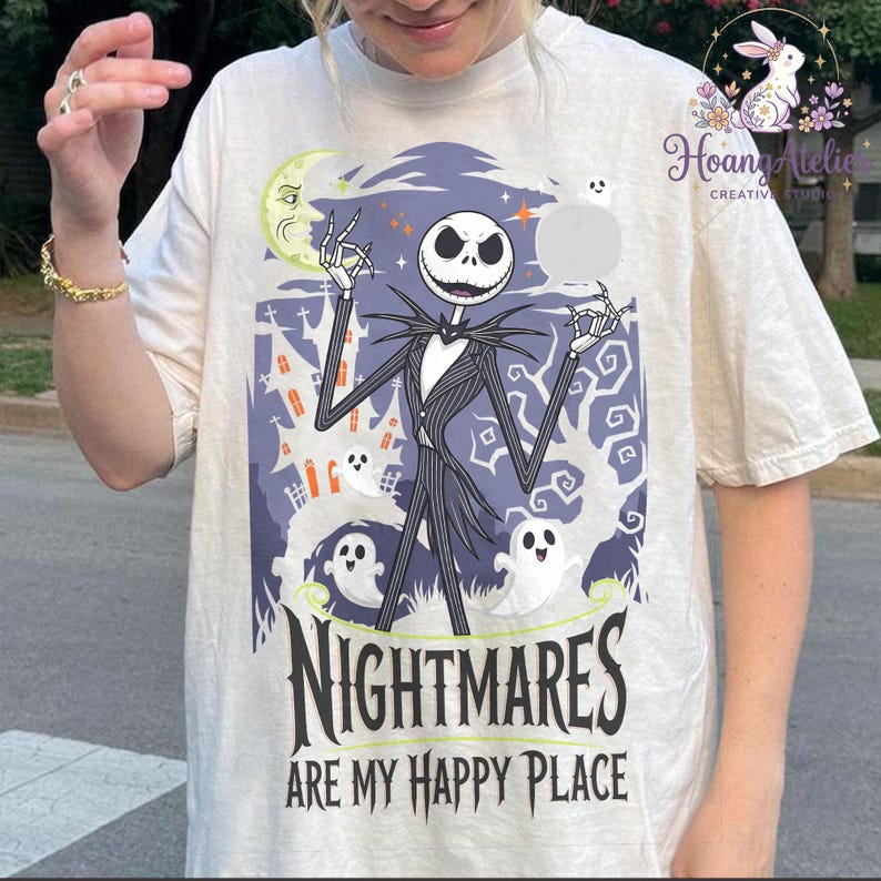 May include: Cream-coloured t-shirt featuring a graphic of Jack Skellington from The Nightmare Before Christmas. The design includes a spooky castle, ghosts, and the text "NIGHTMARES ARE MY HAPPY PLACE" in black.