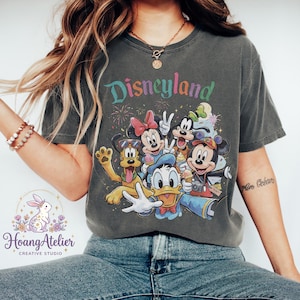 May include: Dark gray t-shirt featuring the word "Disneyland" in colorful text above a graphic of Disney characters including Mickey Mouse, Minnie Mouse, Donald Duck, and Pluto. The shirt has a vintage, worn look.