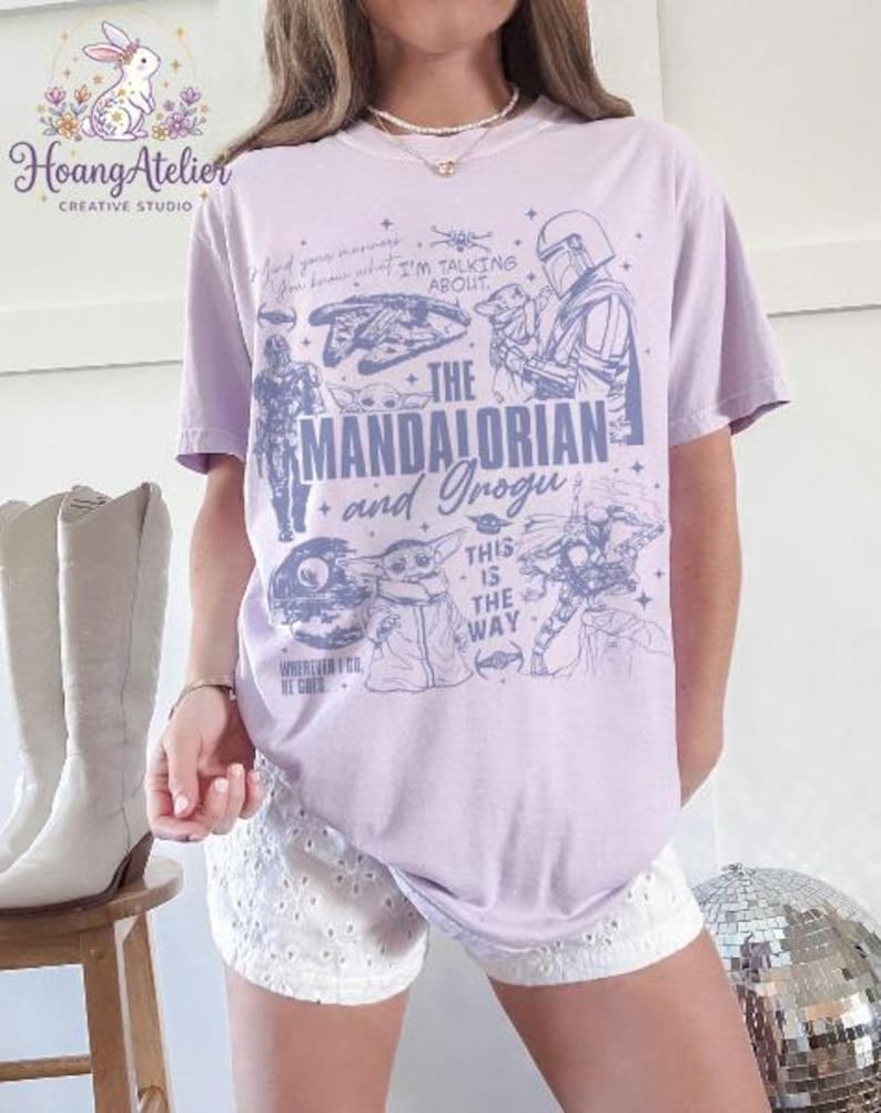Puede incluir: Camiseta lila claro con ilustraciones de "The Mandalorian", incluyendo personajes y frases. El dise&ntilde;o incluye el texto "The Mandalorian and Grogu". La camiseta se usa con pantalones cortos blancos.