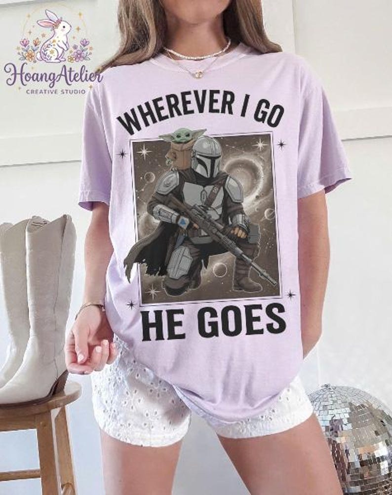 May include: A light purple t-shirt featuring a graphic of a character from a popular science fiction series. The graphic includes the text "WHEREVER I GO HE GOES". The character is holding a weapon, and a small green creature is on his shoulder.
