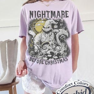 Peut inclure: Un t-shirt lilas avec un graphisme de "L'&Eacute;trange No&euml;l de Monsieur Jack". Le motif comprend le texte "NIGHTMARE BEFORE CHRISTMAS" et des personnages du film. Le t-shirt est &eacute;tiquet&eacute; "Comfort Colors" et "Orchid".