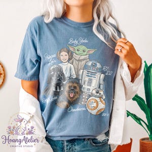 May include: A light blue t-shirt featuring a graphic of Star Wars characters including Princess Leia, Baby Yoda, Darth Vader, Chewbacca, R2-D2, and BB-8. The shirt has the text "Princess Leia", "Baby Yoda", "Darth Vader", "Chewbacca", "R2-D2", and "BB-8".