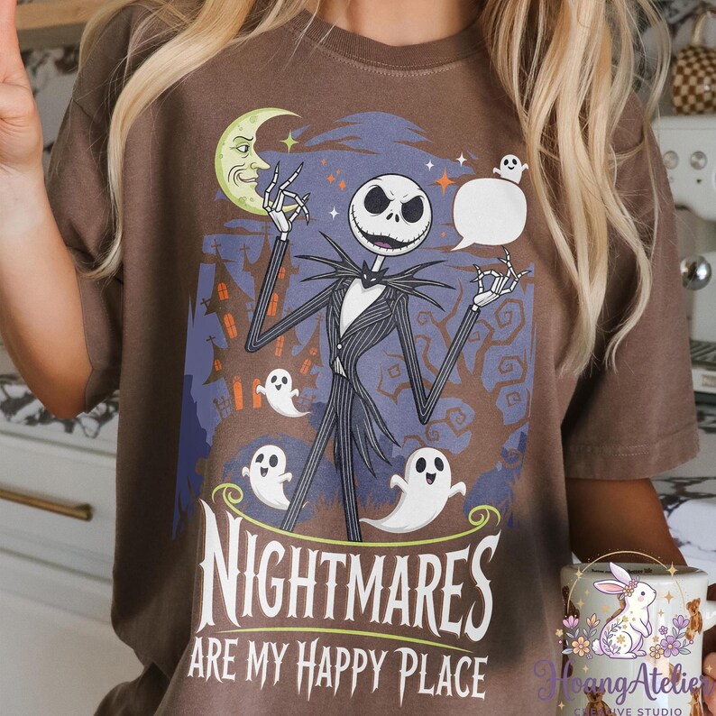 May include: Brown t-shirt with a graphic of Jack Skellington, ghosts, and a moon from The Nightmare Before Christmas. The text reads "NIGHTMARES ARE MY HAPPY PLACE". The design is set against a blue and brown background.