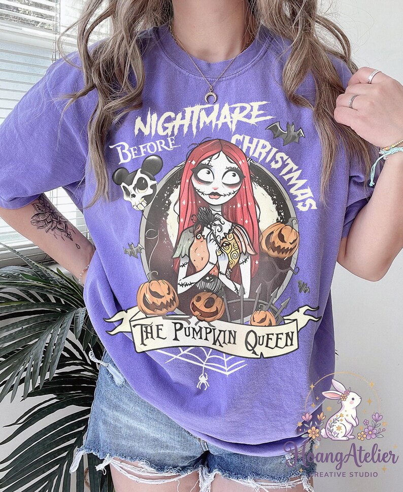 May include: A purple t-shirt featuring a graphic from "The Nightmare Before Christmas." The design includes Sally, pumpkins, and the text "The Pumpkin Queen." The shirt also has the text "Nightmare Before Christmas" in a circular design.