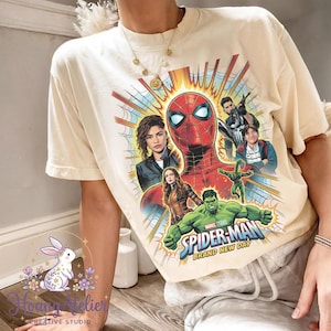 May include: Cream-colored t-shirt featuring a vibrant graphic of Spider-Man and other Marvel characters. The design includes the text "Spider-Man Brand New Day" in a dynamic, comic-book style. The shirt has a classic crew neck and short sleeves.