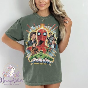 May include: Olive green t-shirt featuring a graphic of Spider-Man and other Marvel characters. The design includes the text "SPIDER-MAN BRAND NEW DAY". The shirt has a crew neck and short sleeves.