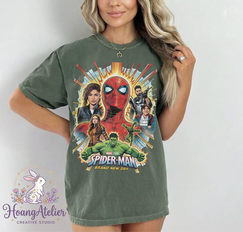 May include: Olive green t-shirt featuring a graphic of Spider-Man and other Marvel characters. The design includes the text "SPIDER-MAN BRAND NEW DAY". The shirt has a crew neck and short sleeves.