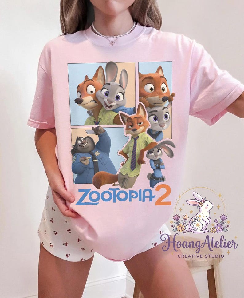 K&ouml;nnte beinhalten: Hellrosa T-Shirt mit einem Comic-Strip-Design mit Charakteren aus dem Animationsfilm "Zoomania". Das Design zeigt einen Fuchs, ein Kaninchen und andere Charaktere. Der Text "Zoomania 2" ist ebenfalls sichtbar.
